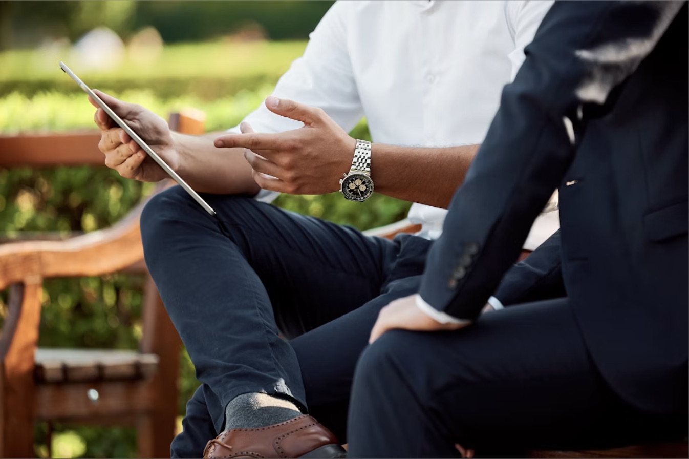 Two people reviewing a tablet together outdoors on a bench